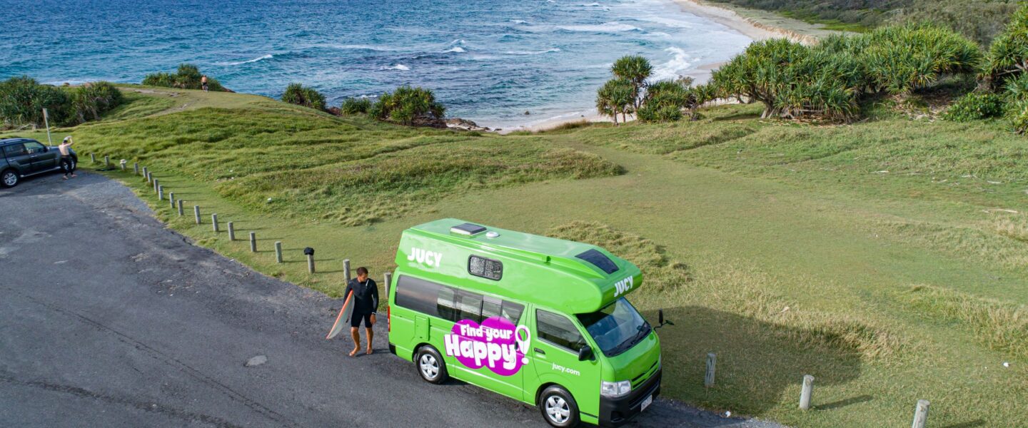 Jucy Condo Australië man met surfplank en de zee op de achtergrond