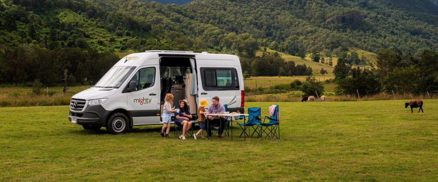 Gezin met jonge kinderen zit buiten aan tafel voor een Mighty Double Down camper