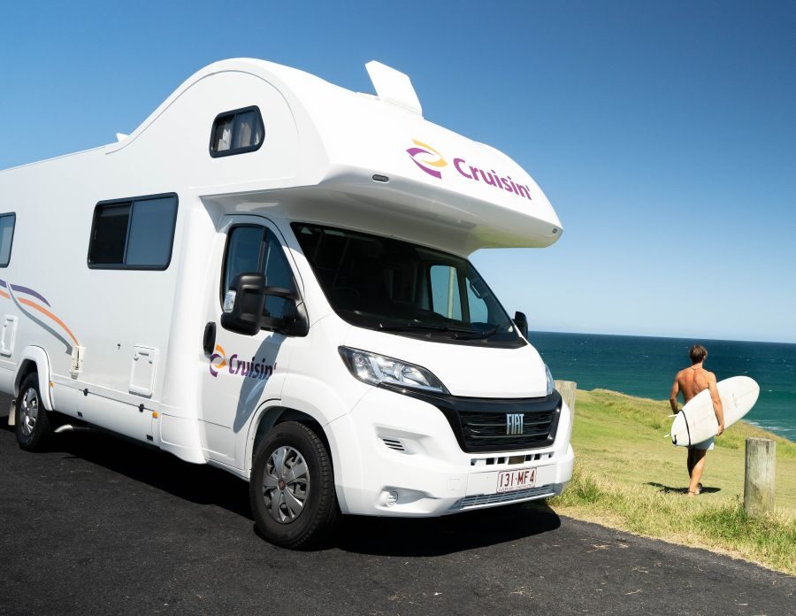 Cruisin' 6 Berth Deluxe staat geparkeerd op het strand, iemand gaat surfen