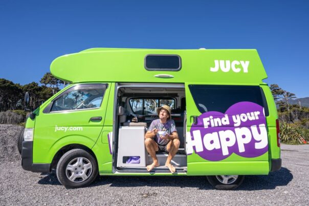 Man eet zittend uit een bakje in de zijdeur van de Jucy Chaser