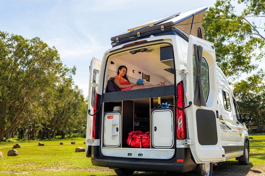 Vrouw leest op bed van Britz Voyager camper met achterdeur open