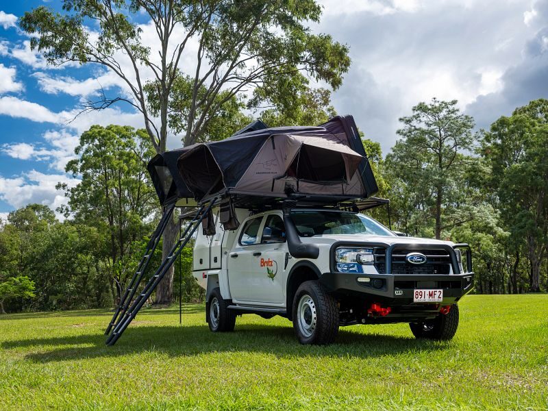 Britz Warrior 4WD staat geparkeerd op het gras met daktenten uitgeklapt en ladders