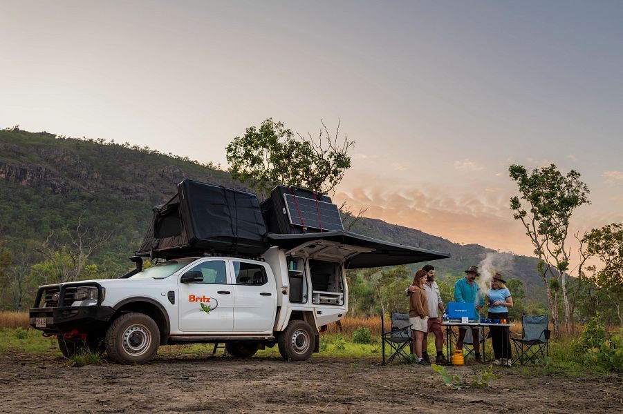 Vrienden koken samen buiten op het draagbare gastoestel van de Britz Warrior 4WD bij schemering