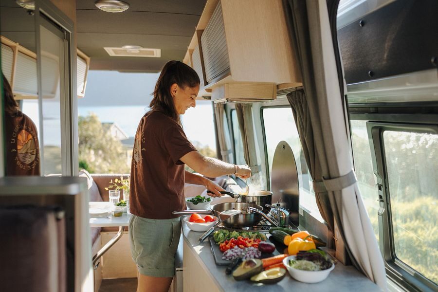 Een vrouw staat in de keuken te koken in de Britz Venturer camper in Nieuw-Zeeland