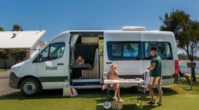 Een koppel zit op de campingstoelen voor de Maui Ultima Plus camper waar een kind binnen op het eenpersoonsbed ligt