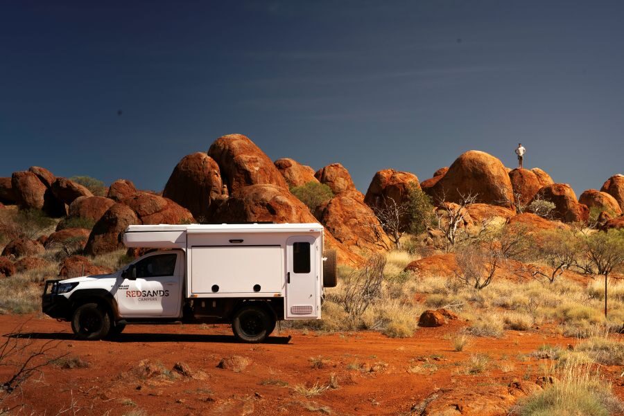 De camperreiziger is uit de RedSands camper gestapt om bovenop een rotsblok van het uitzicht te genieten