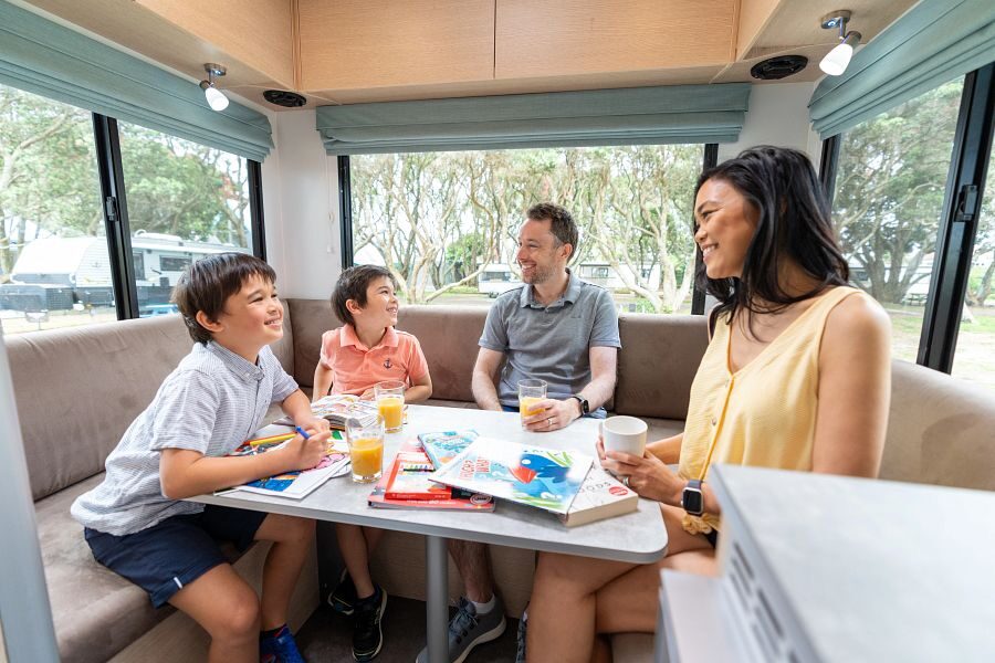 Een gezin met twee kinderen zit achterin de Maui Beach camper in de zithoek wat te drinken terwijl de kinderen aan het kleuren zijn