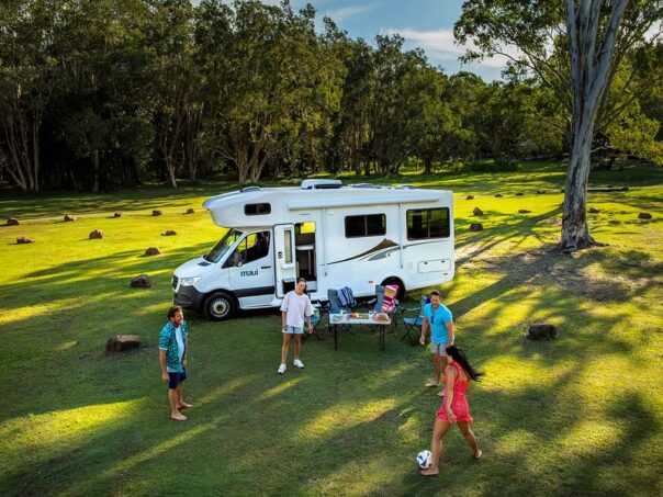 Een gezin is aan het voetballen voor de Maui Sunset Australië camper die geparkeerd staat op het gras