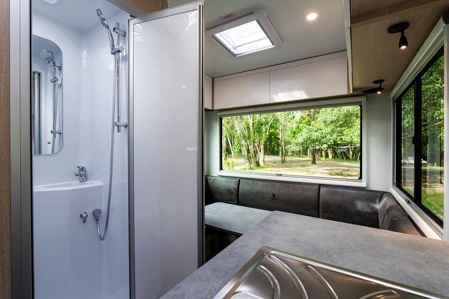 De badkamerdeur staat open met de wasbak en douche met daarnaast de ruimte zithoek achterin de Maui Sunset camper