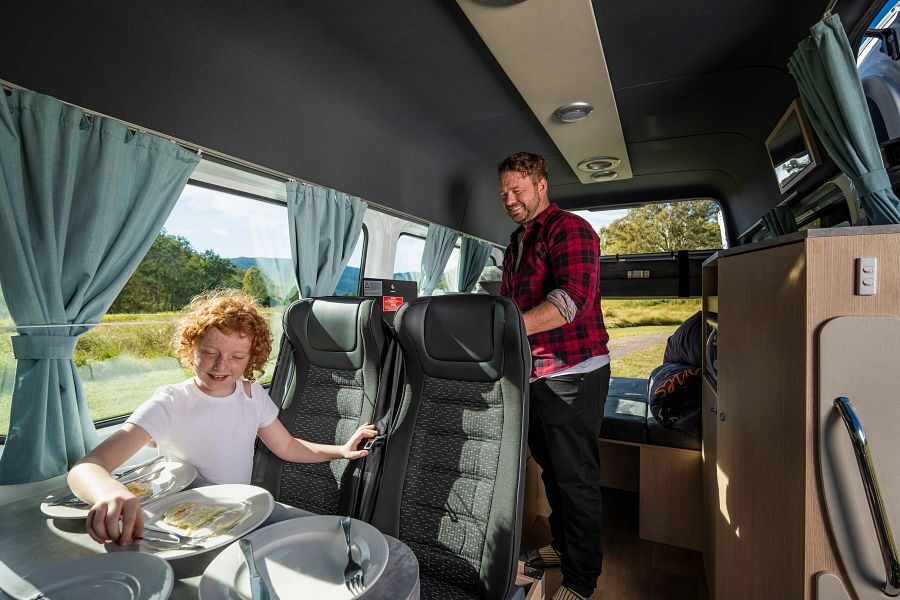Een vader is aan het koken terwijl zijn kind aan tafel zit in de Mighty Double Down camper in Australië