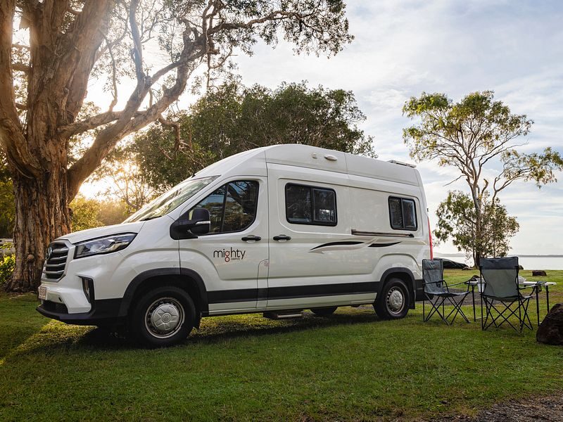 De Mighty Duo camper van de zijkant geparkeerd op het gras met twee campingstoelen en een tafel ernaast