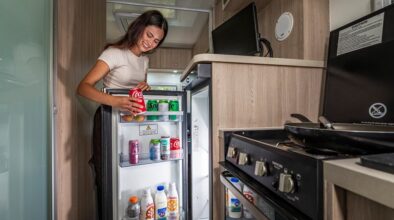 Een vrouw pakt een blikje drinken uit de koelkast in de keuken van de Mighty Big Six camper