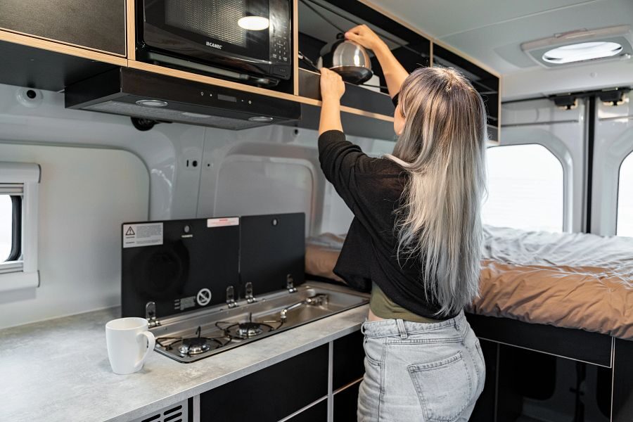 Een vrouw pakt een fluitketel uit de opbergruimte boven de keuken in de Mighty Lite HiLITE camper in Nieuw-Zeeland