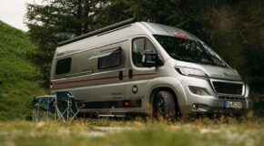 De McRent Urban Plus camper staat geparkeerd op een grasveld met campingstoelen aan de zijkant van de camper