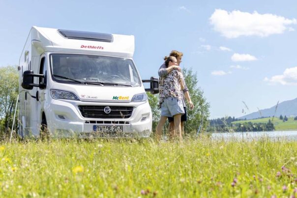 Een stel staat schuin voor de McRent Kiwi Compact camper te genieten van het uitzicht
