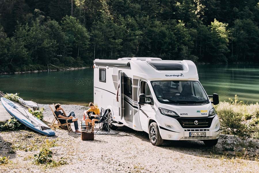 Een stel zit aan de zijkant van de McRent Family Standard camper gitaar te spelen met op de achtergrond een meer