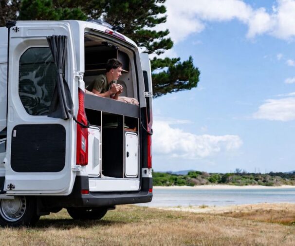Man ligt op het bed van de Apollo Hitop camper met de achterdeur open en kijkt naar buiten