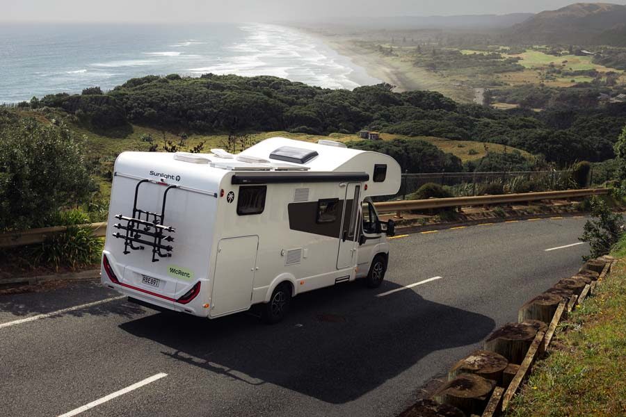 De McRent Family Luxury motorhome rijdend op een geasfalteerde bergweg door Nieuw-Zeeland vanaf de achter- en zijkant gezien