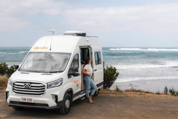 Vrouw staat tegen geopende zijdeur van Britz Trailblazer langs de Great Ocean Road