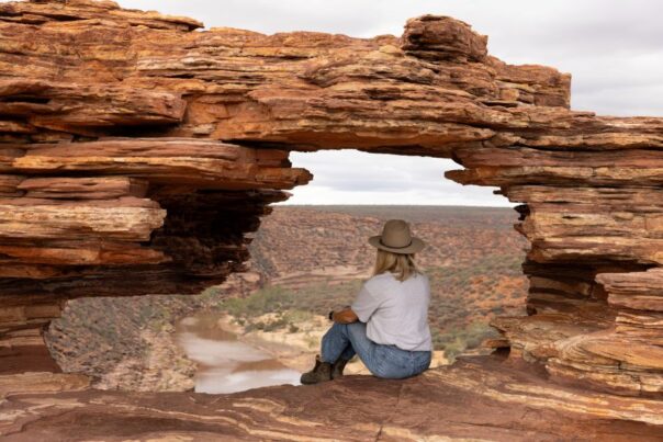 Vrouw zit in het gat van Natures Window uit te kijken over de Murchison River in Kalbarri National Park