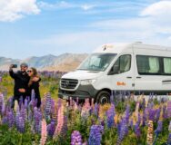 Stel maakt een selfie voor een Britz camper met lupines op de voorgrond