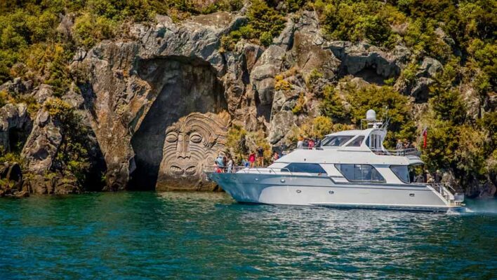Een boot met toeristen vaart over Lake Taupo langs de Maori rock carving