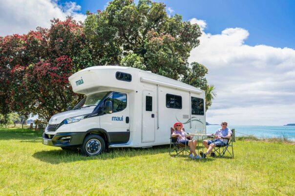 Een koppel zit voor de Maui Beach camper in de omgeving van Auckland