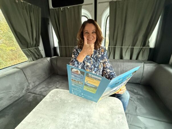 Karin zit in Maui Ultima Plus camper in Woerden met brochure Campers Down Under in haar hand en steekt duim omhoog