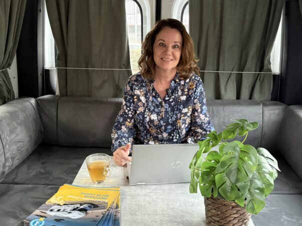 Karin zit in Maui camper met kop thee en laptop voor webinar Australië en Nieuw-Zeeland