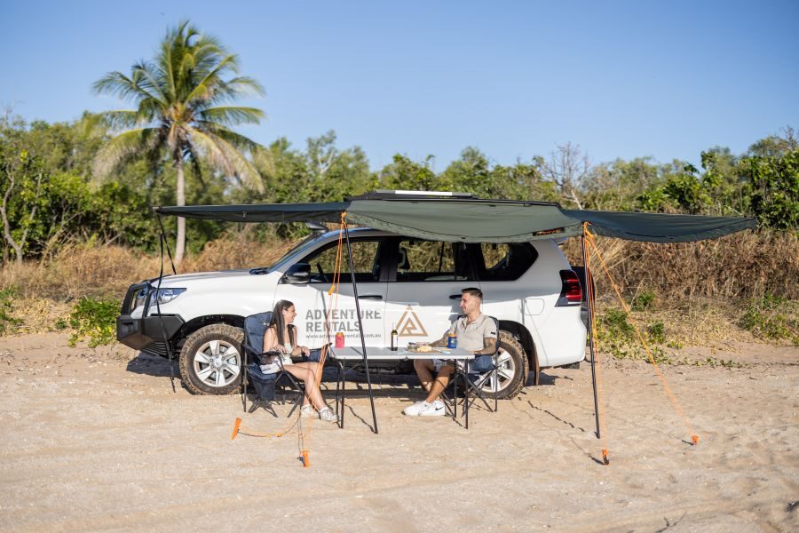 Adventure Rentals Toyota Prado 4WD camper stel zit aan een campingtafel oinder de luifel